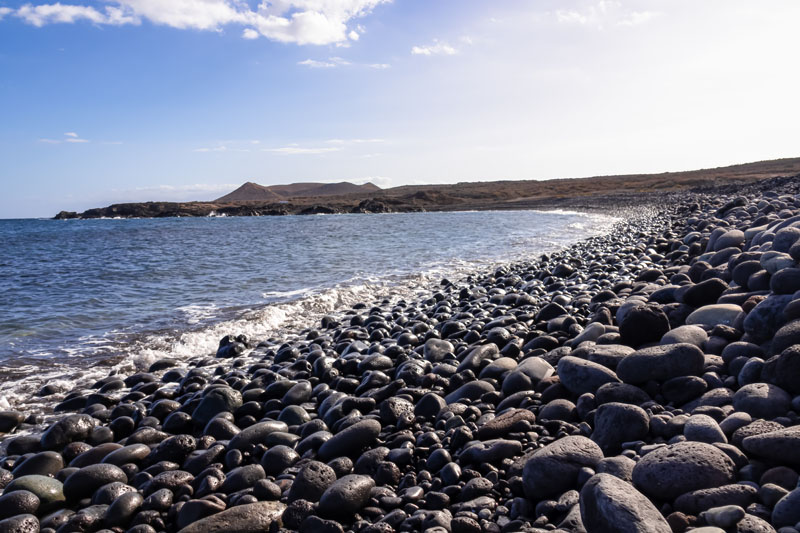 Panoramic view on black stone pebble beach Playa Colmenares near Amarilla, Golf del Sur, Tenerife, Canary Islands, Spain, Europe. Montana Amarilla in the back. Tranquil waves from the Atlantic Ocean